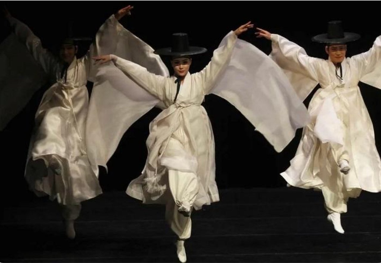 Traditional Korean ritual dancers in white hanbok, arms raised mid-movement, high-key ethereal black and white